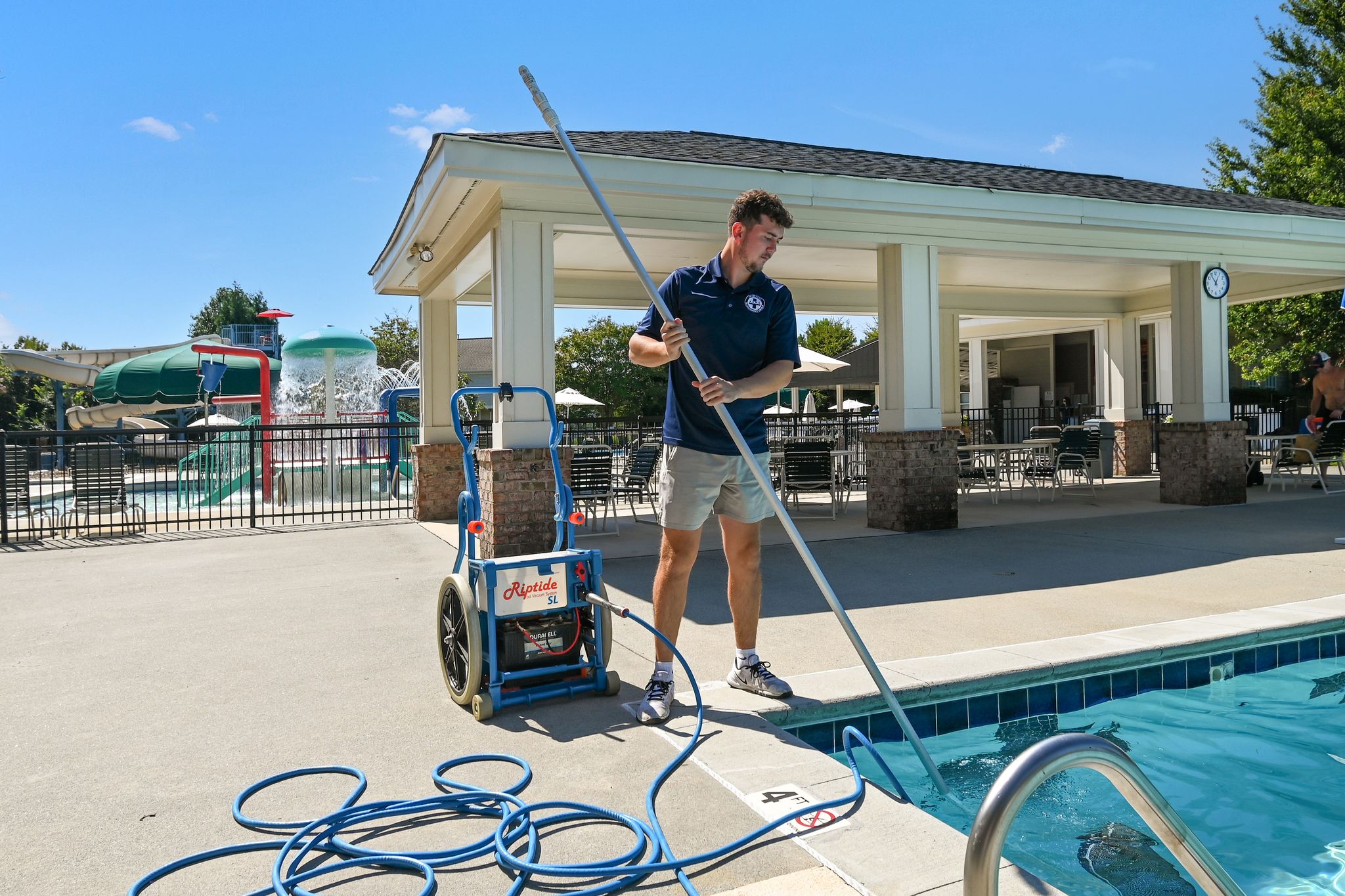 male pool operations staff member using cleaning device to clean a community pool