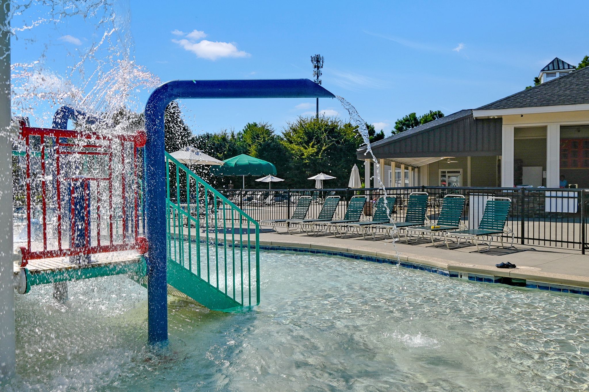 Water coming out of a blue tube next to a jungle gym spraying water in a municipal pool
